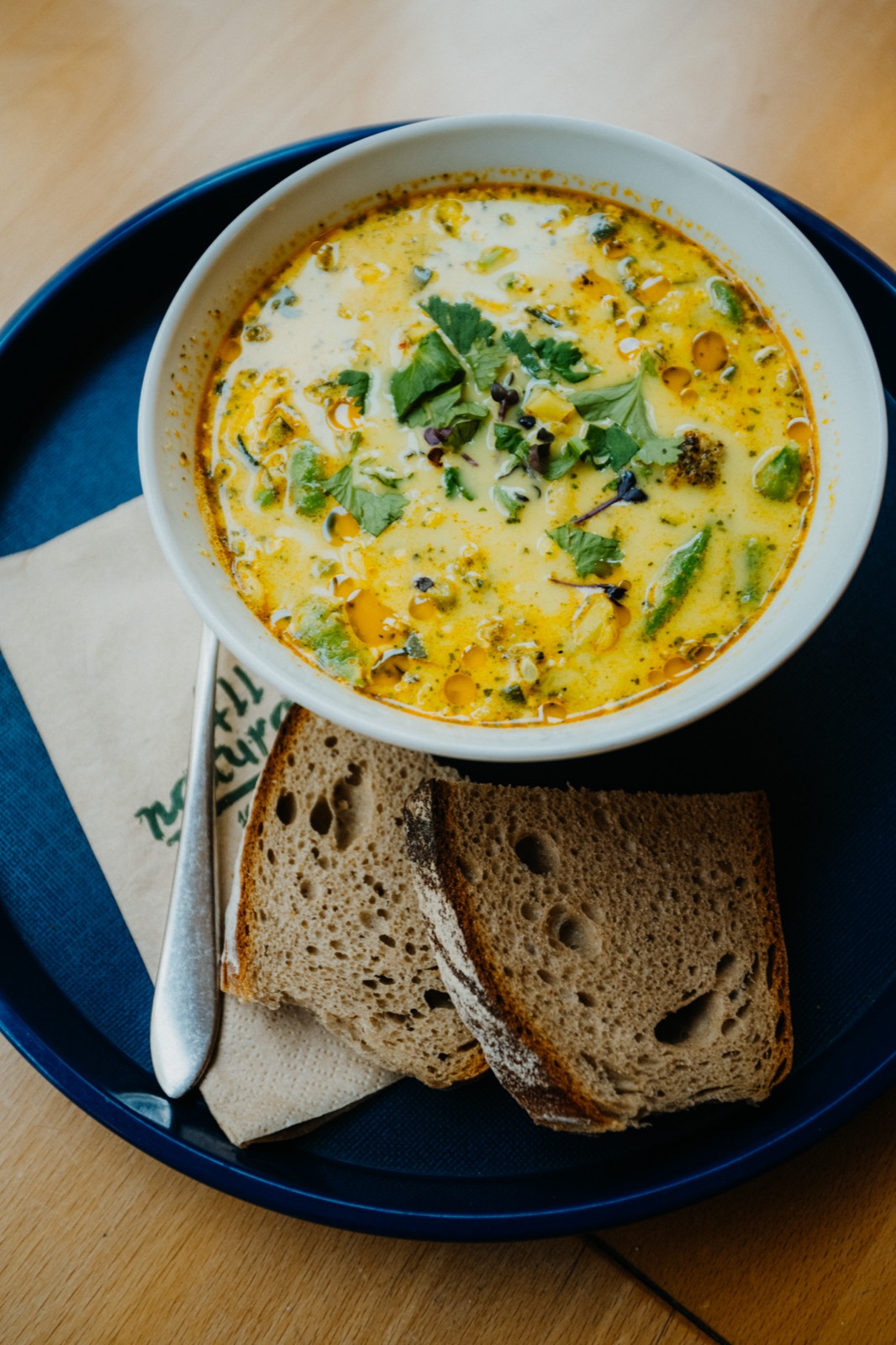 Gelbe Suppe mit Kräutern und Brot auf einem Tablett